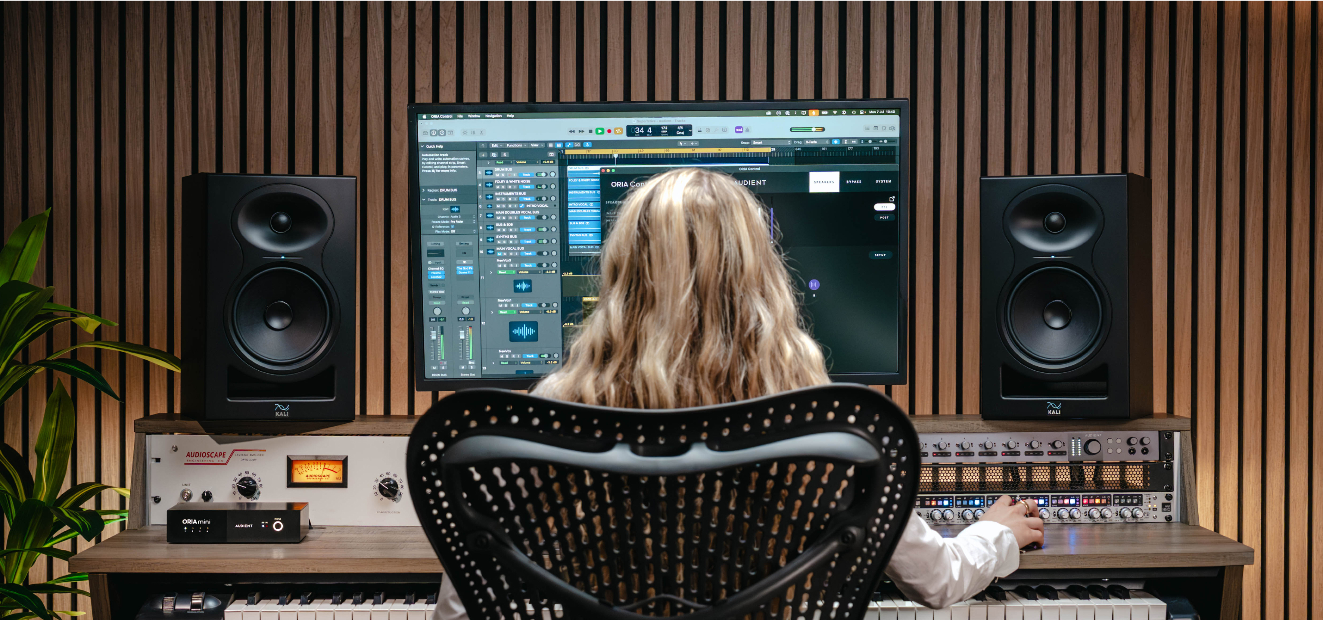 Home studio with ORIA Mini on desk; engineer mixing in Logic Pro between black Kali monitors and Audioscape VU meter.